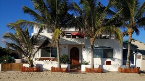 A beachfront property with a white building, palm trees, and a sandy beach. - Drake Inn (Puerto Villamil)
