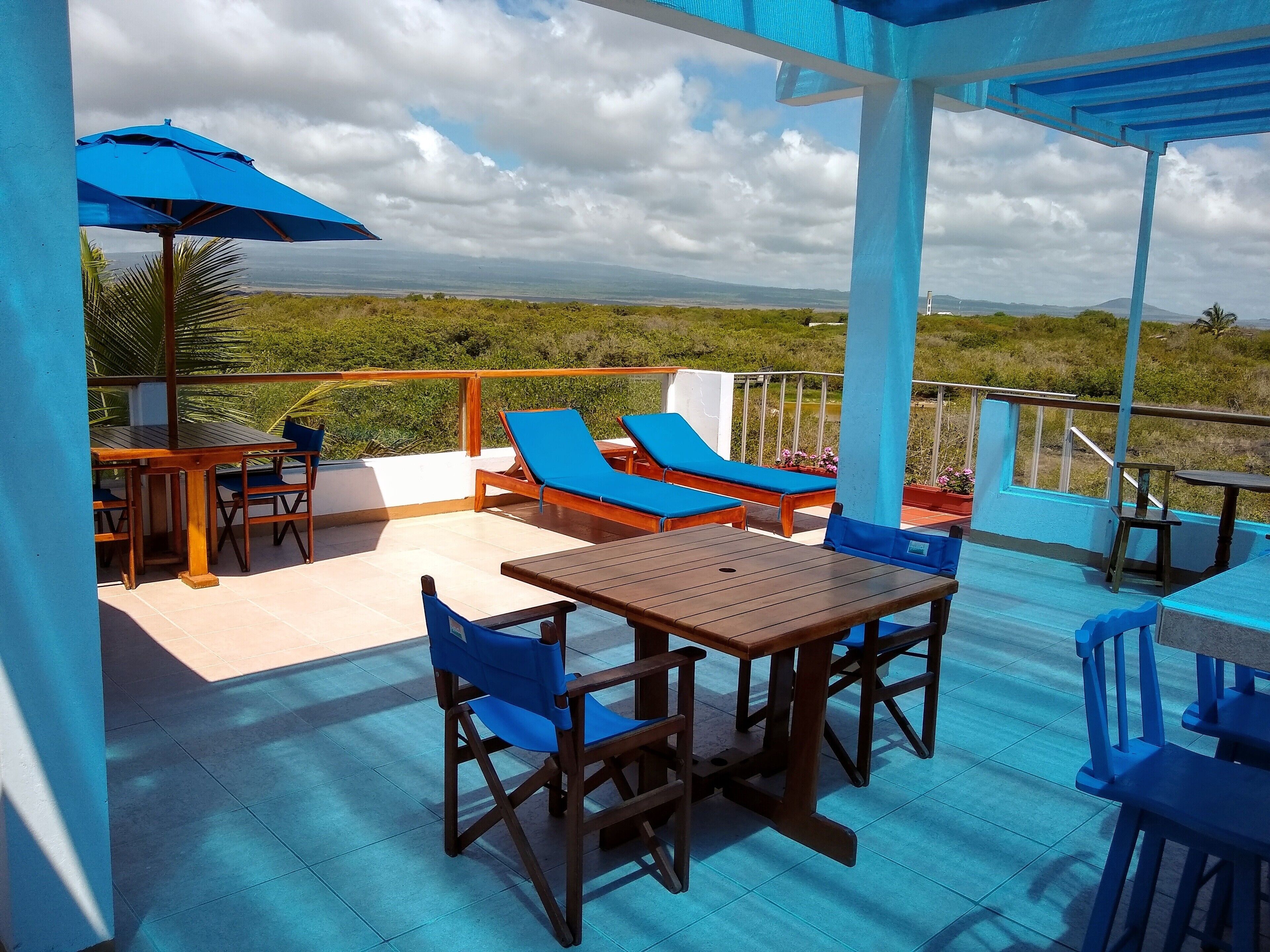 Una terraza con mobiliario de madera, cojines azules y vista al paisaje.