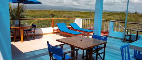 Una terraza con mobiliario de madera, cojines azules y vista al paisaje.