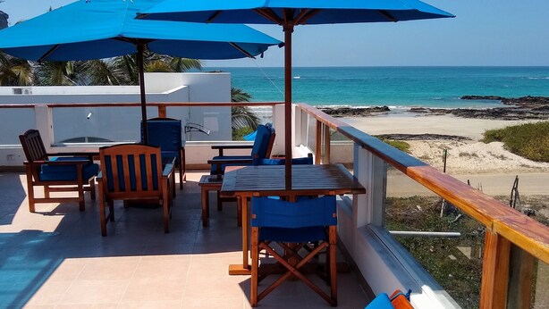 A poolside area with blue lounge chairs and umbrellas, overlooking a beach. - Drake Inn (Puerto Villamil)