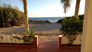 A beach view from a covered walkway with palm trees and a tiled floor. - Drake Inn (Puerto Villamil)