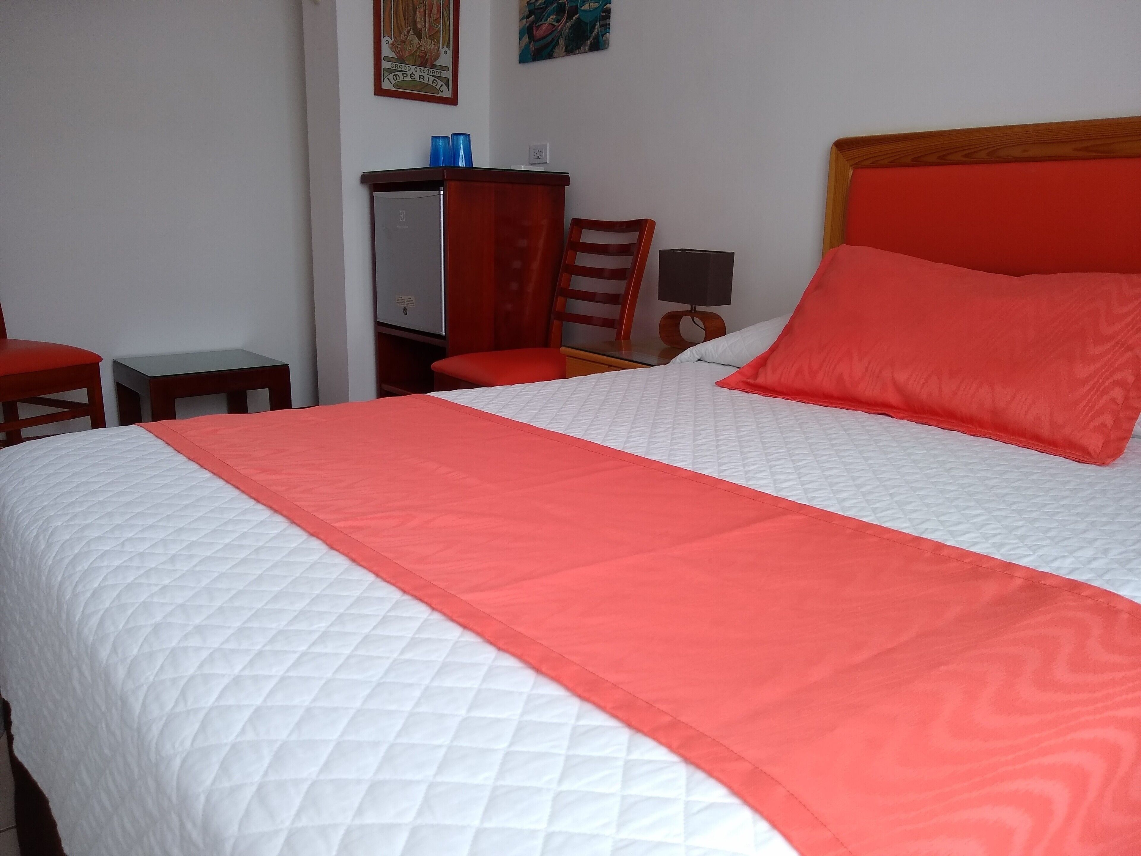 A neatly made bed with a white and red bedspread, a red pillow, and a wooden headboard.