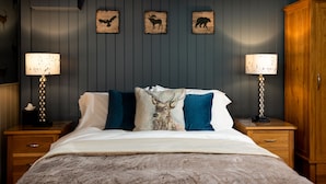 Une chambre à coucher comprenant un lit, deux tables de chevet avec des lampes, une armoire en bois et des œuvres d’art sur le thème des animaux accrochées au mur.