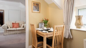 Un coin repas avec une table en bois dressée pour deux personnes, un vase rempli de fleurs et un tableau accroché au mur.