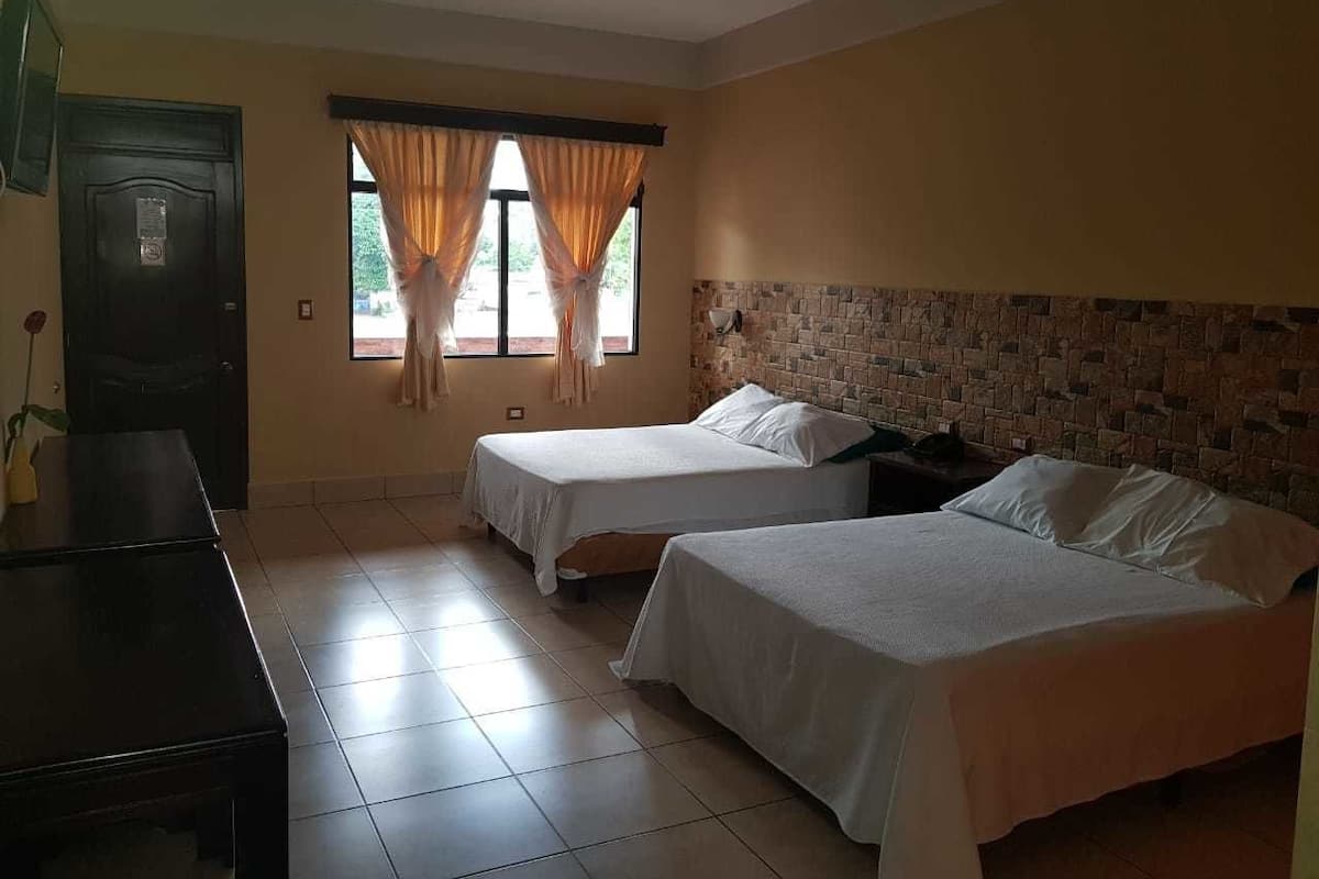 A hotel room with two single beds, a wooden desk, a tiled floor, and a brick-patterned wall.