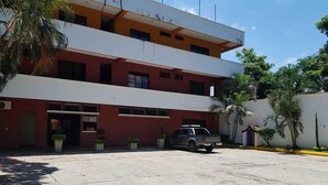 Un edificio de varios pisos con fachada roja y blanca, un área de estacionamiento techada y un vehículo estacionado.