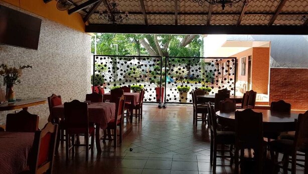 Un comedor interior con varias mesas y sillas, una pared de ladrillo y vistas al jardín exterior.