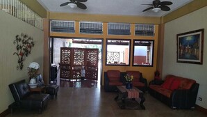 Un salón amplio con dos sofás, una mesita de centro y una televisión. Hay ventiladores de techo, un elemento decorativo en la pared y una ventana con vistas.