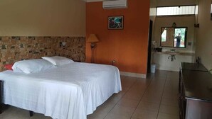 Habitación de hotel con cama, lámpara, baño con espejo y kitchenette.