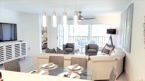 A modern living room with a glass dining table, sofas, and a TV.