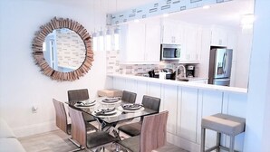 A modern kitchen with white cabinets, stainless steel appliances, and a glass dining table with chairs.