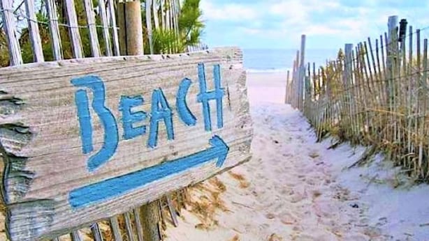 A wooden sign with the word "Beach" and an arrow pointing to the right, indicating the direction to the beach.