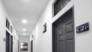 A hallway with a tiled floor, white walls, and dark doors. There is a sign on the wall that reads "C24". - Hotel San José (San José)