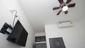 A room with a ceiling fan, a mounted flat-screen TV, and an air conditioning unit. - Hotel San José (San José)