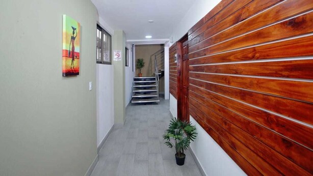 A hallway with a wooden wall, a staircase, and a potted plant. - Hotel San José (San José)