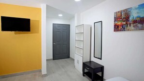 A hotel room with a television, a door, a white wardrobe, a small table, and a painting on the wall. - Hotel San José (San José)