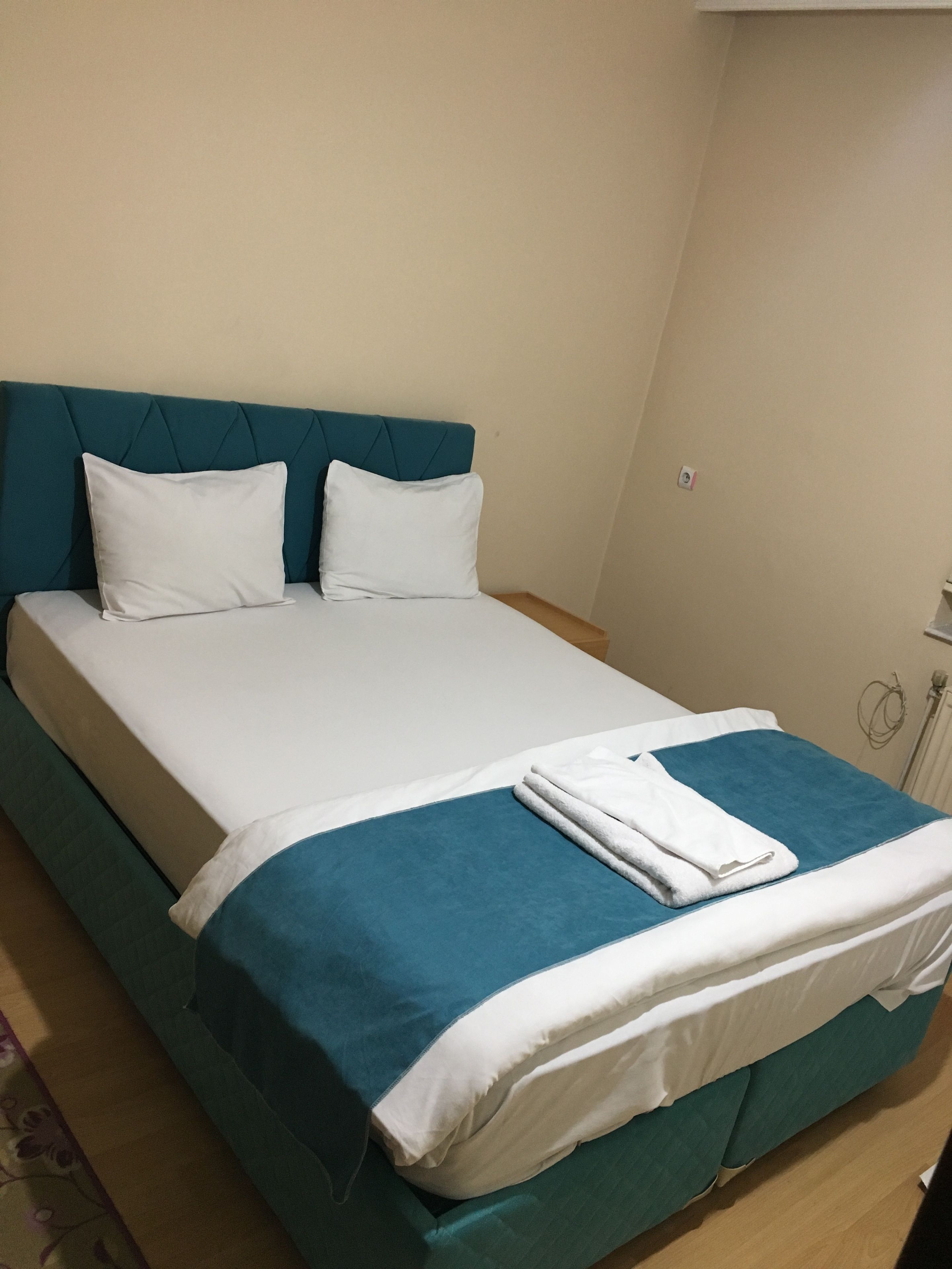 A neatly made bed with a teal headboard, white bedding, and a folded white towel.