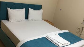 A neatly made bed with a teal headboard, white bedding, and a folded white towel.