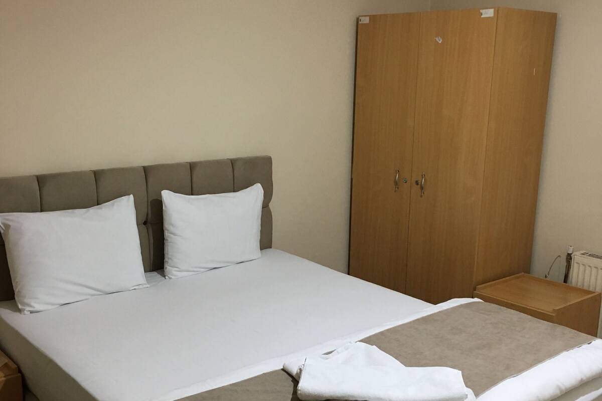 Ein ordentlich bezogenes Bett mit weißer und beiger Bettwäsche, ein Holzschrank und ein kleiner Nachttisch.