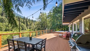 A deck with a grill, outdoor seating, and string lights. - Diamond on the Sky: Riverfront mountain lodge w/ views, AC & WiFi (Skykomish)