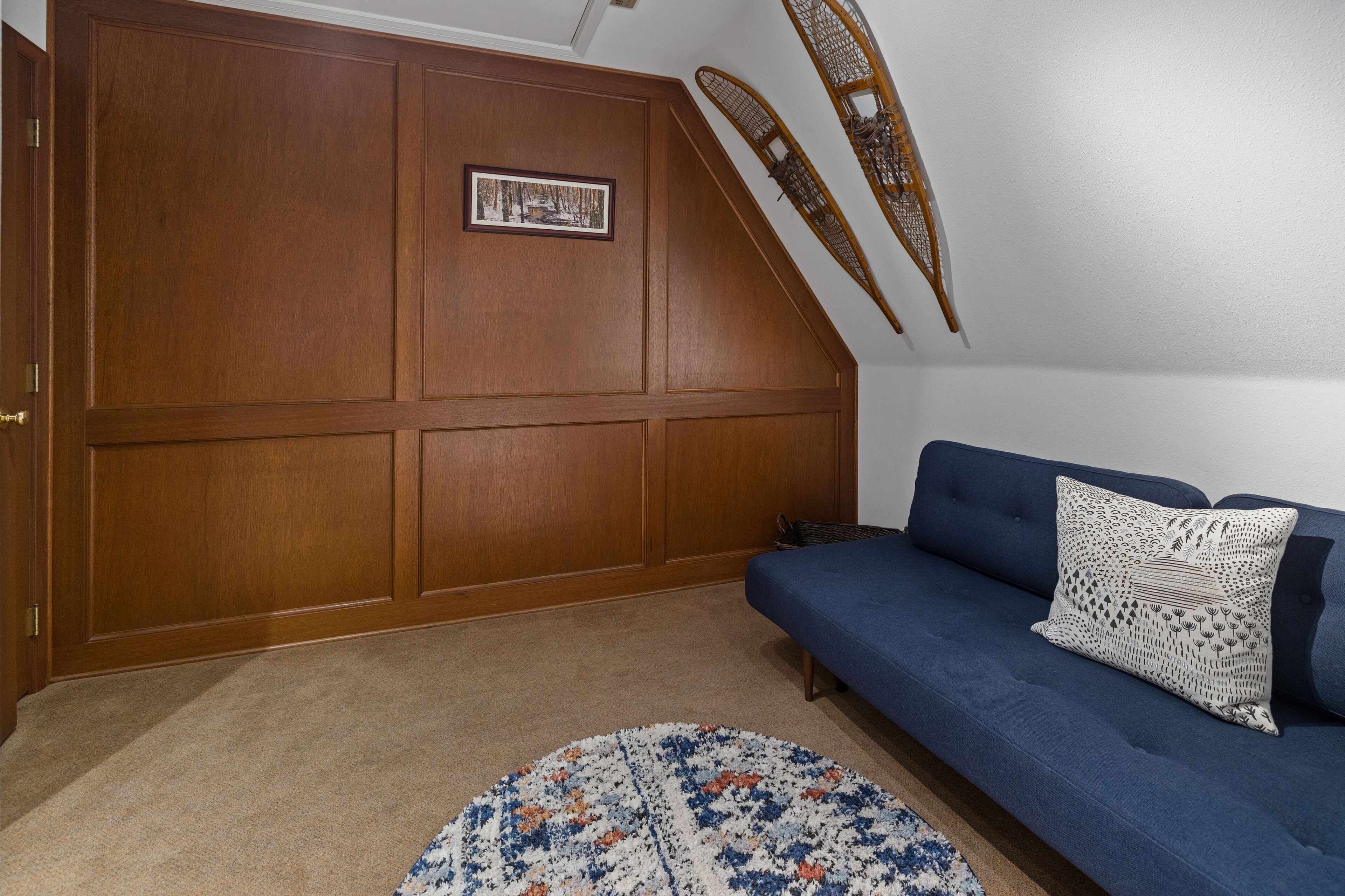 Una habitación con un sofá azul, un tapete estampado y una pared de paneles de madera con un cuadro enmarcado.