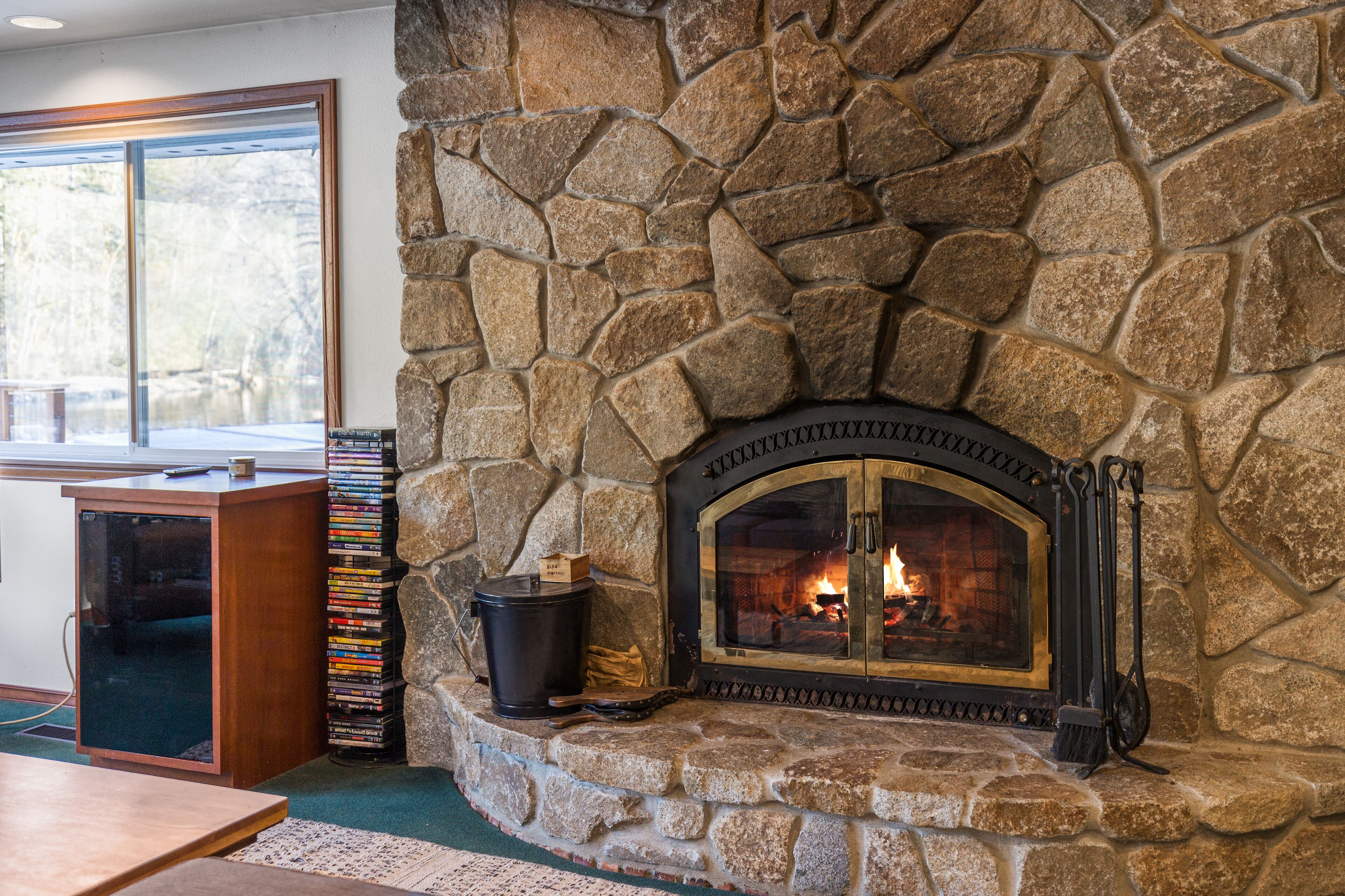 A stone fireplace with a fire, a wooden table, and a stack of books beside it.