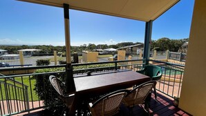 Ein Balkon mit Tisch und Stühlen, der auf einen eingezäunten Bereich mit Gebäuden und Grünflächen blickt.