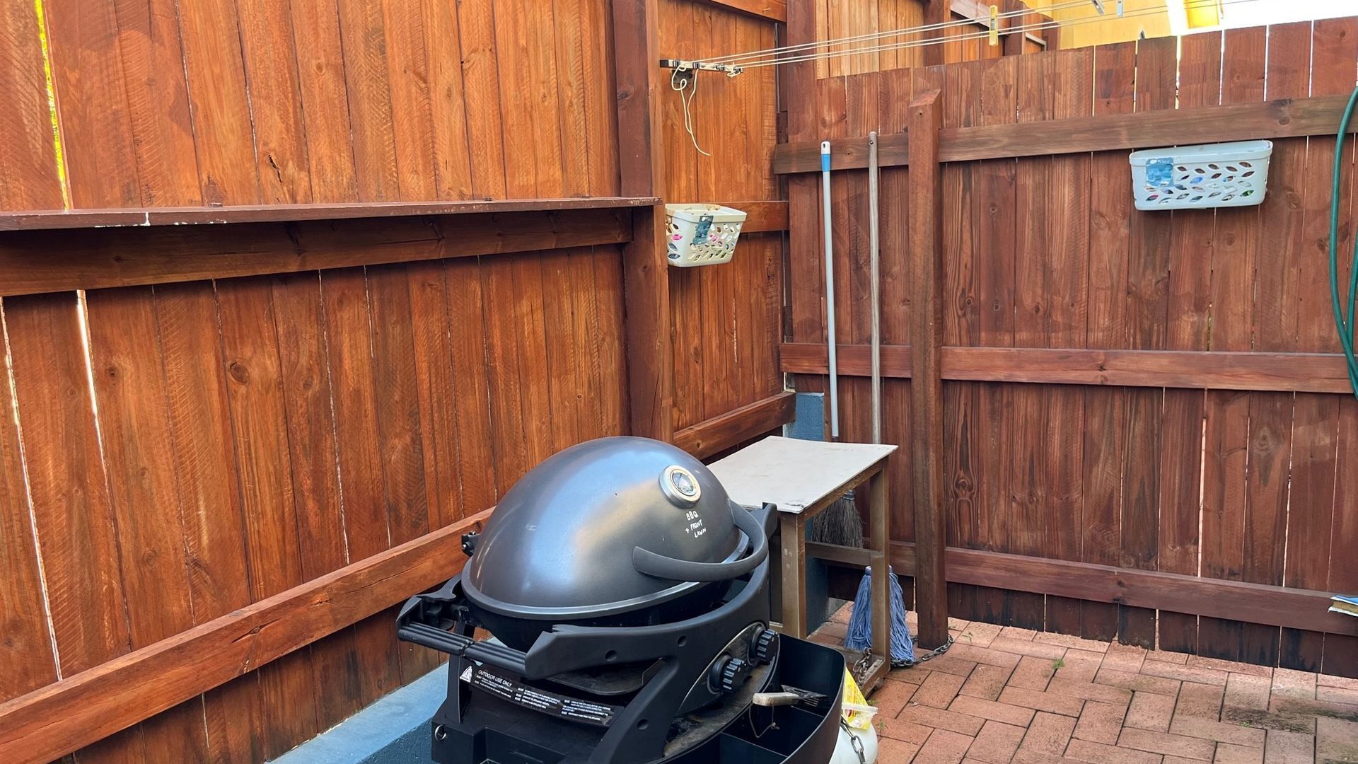 A barbecue grill in a backyard with a wooden fence and a table.