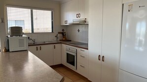 Eine Küche mit weißen Schränken, einem Herd, einer Spüle und einem Fenster mit Jalousien.