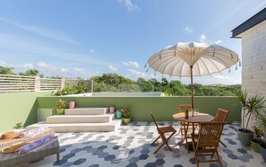 Terraza en la azotea con una mesa, sillas, un paraguas grande y plantas en macetas.