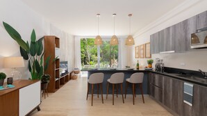 Una cocina moderna con una isla central, taburetes de bar, iluminación colgante y vistas a zonas verdes.