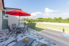 Una terraza en la azotea con una mesa de comedor, sillas, un paraguas rojo y una botella de champán.