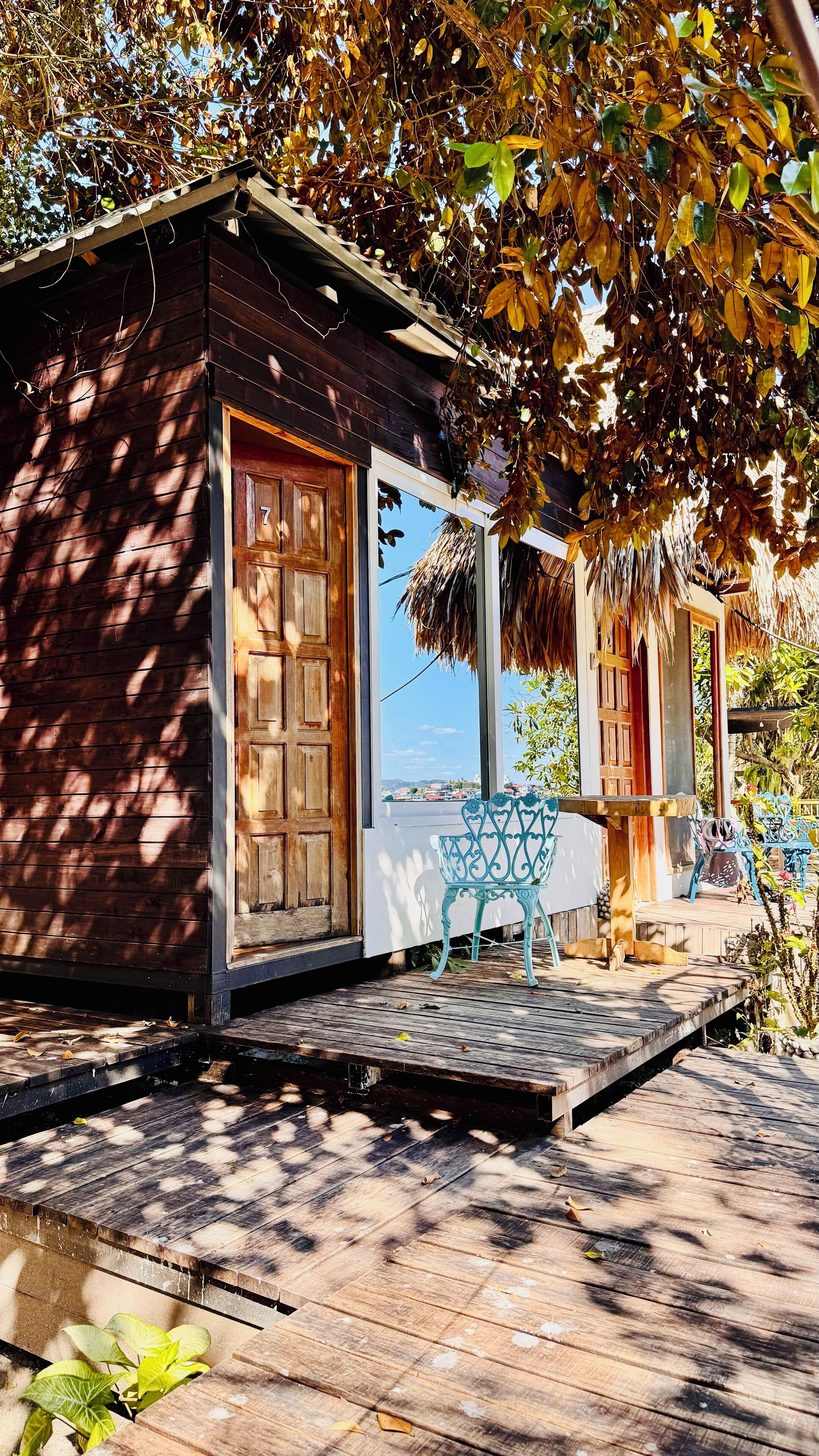 Eine Holzhütte mit Veranda, einem blauen Stuhl und Blick auf eine Stadt im Hintergrund.