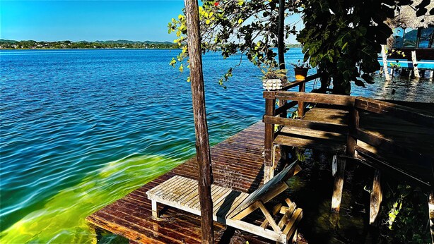 Une jetée en bois s’étendant dans un lac aux eaux d’un bleu limpide, avec un banc et des plantes en pot.