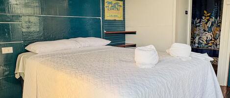 A single bed with a white bedspread in a room with wooden flooring and a teal-colored wall.