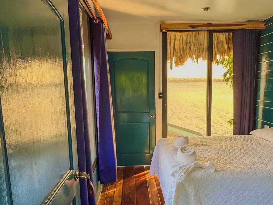 A room with a bed, wooden floor, and a view of the beach.