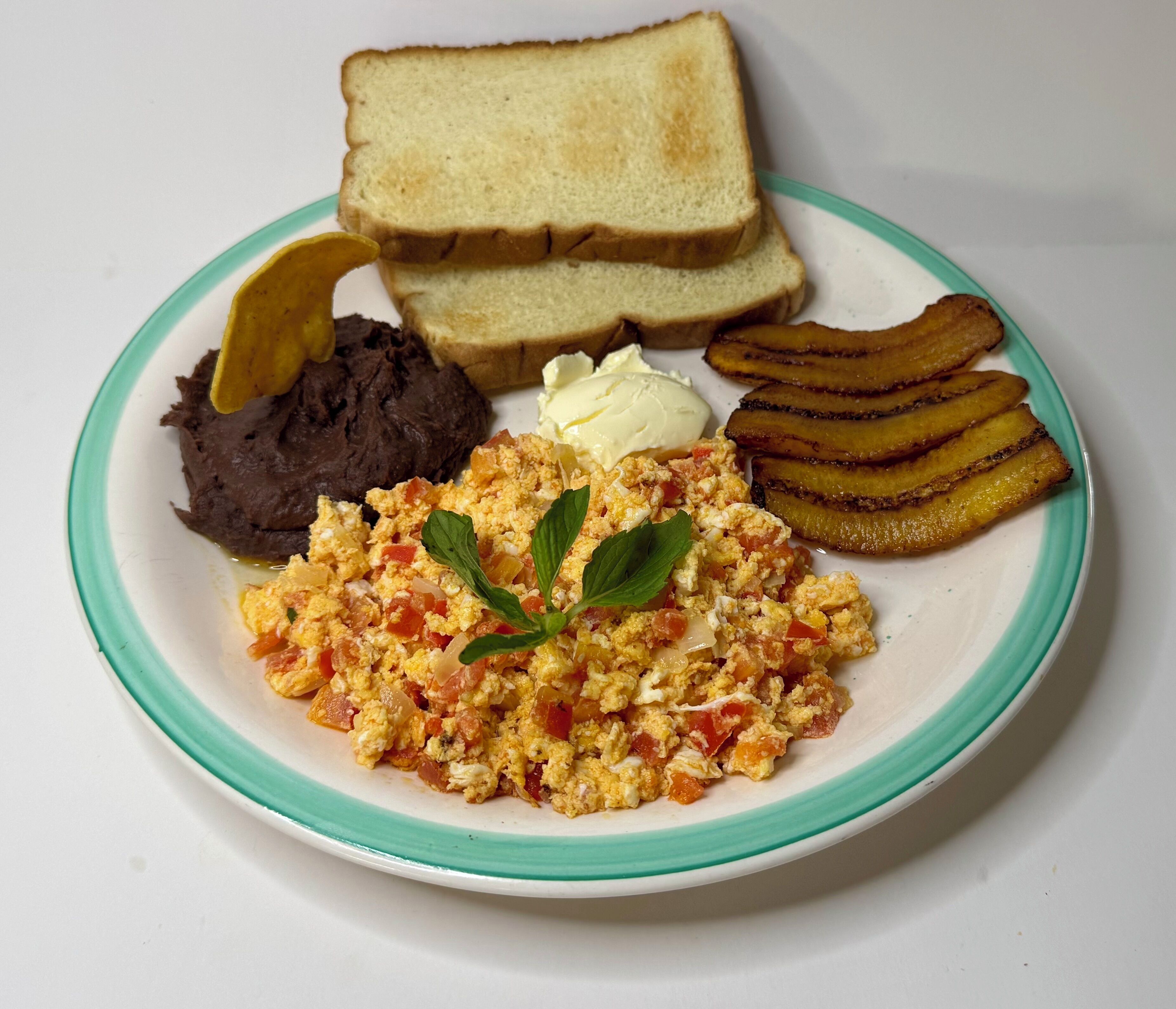Une assiette contenant des œufs brouillés, des toasts, des haricots noirs et des bananes plantains frites.