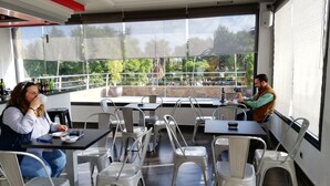 An outdoor café with tables and chairs, large windows with a view of greenery, and a modern interior design. - Hotel LB Lebrija by MA 22 Puntos (Lebrija)