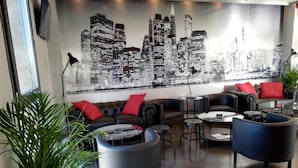 A modern lounge area with a cityscape mural, leather sofas, and round tables. - Hotel LB Lebrija by MA 22 Puntos (Lebrija)