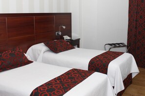 A hotel room with two beds, each with a white bedspread and red patterned pillows. There is a wooden headboard, a bedside table with a lamp, and a black chair. - Hotel LB Lebrija by MA 22 Puntos (Lebrija)