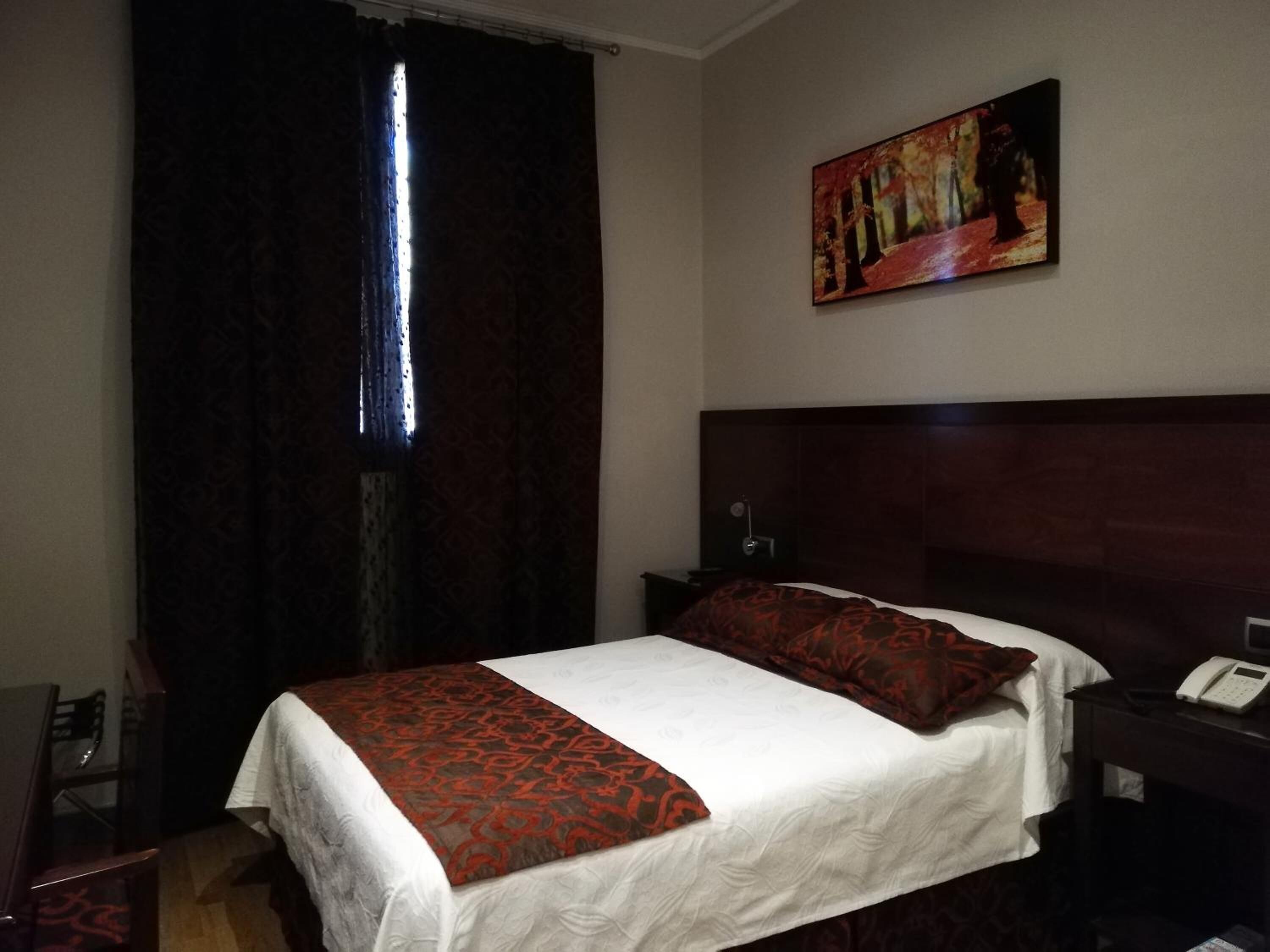 Une chambre d’hôtel avec un grand lit, une table de chevet avec un téléphone, un tableau au mur et une fenêtre avec des rideaux.