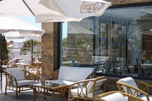 Un área de estar al aire libre con mobiliario de mimbre y cojines blancos, con sombrillas de Coca-Cola.