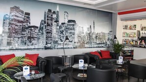 A modern lounge with black leather sofas, round tables, and a cityscape mural on the wall. - Hotel LB Lebrija by MA 22 Puntos (Lebrija)