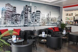 Un salón moderno con sofás de cuero negro, mesas redondas y un mural con vista a la ciudad.