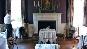 A dining room with a fireplace, dining tables, chairs, and a painting on the wall. - Planters Inn (Savannah)