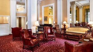 A luxurious hotel room with a red carpet, leather armchairs, a sofa, and a large mirror reflecting the room. - Planters Inn (Savannah)