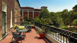 A balcony with outdoor seating, a brick building, and a view of a campus with trees and a building in the background. - Planters Inn (Savannah)