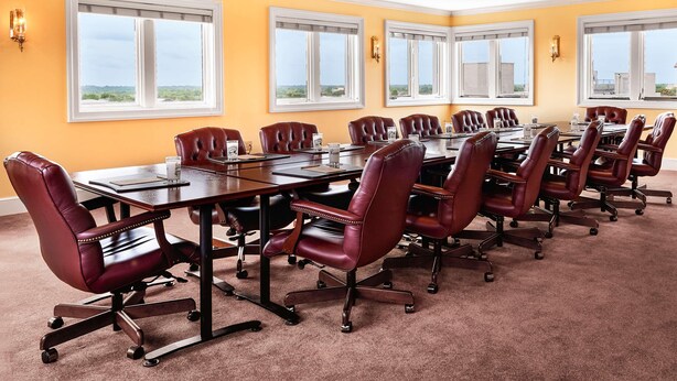 A conference room with a long table and multiple leather chairs, large windows with white frames, and a yellow wall. - Planters Inn (Savannah)