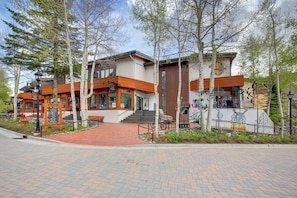 Een modern gebouw met een met baksteen bestraat pad dat naar de ingang leidt, omgeven door bomen.