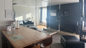 Moderni hotellihuone, jossa on puinen ruokapöytä, sohva, televisio ja liukuovi, joka johtaa parvekkeelle.